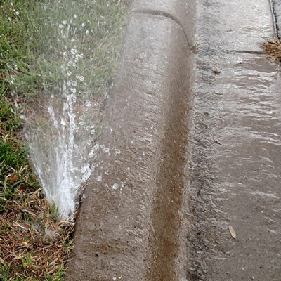 Wasted water running into the street from a broken irrigation head